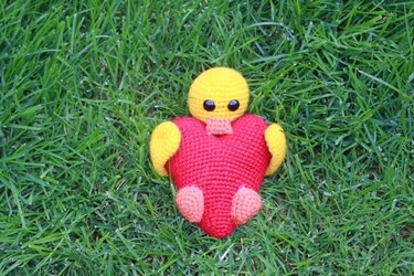 Gehäkeltes gelbes Küken-Amigurumi mit rotem Herz auf Gras