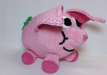 Rosa gehäkeltes Amigurumi-Glücksschwein mit Schlappohren, aufgesticktem Gesicht und grünem Kleeblatt