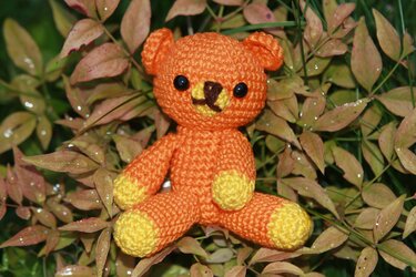 Nahaufnahme eines sitzenden gehäkelten Teddybären in Orange mit gelben Pfoten