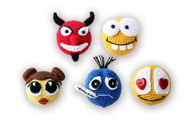 Nahaufnahme mehrerer gehäkelter Emoji-Amigurumi mit unterschiedlichen Augen- und Mundgestaltungen