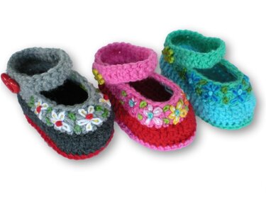 Drei gehäkelte Mary‑Jane‑Babyschuhe in Grau, Rosa und Türkis mit Blumenapplikationen und Riemchen.