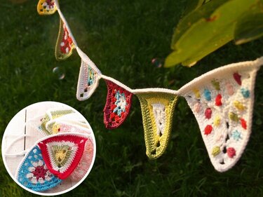 Bunte gehäkelte Wimpelkette mit dreieckigen Wimpeln in Rot, Blau, Gelb und Grün vor grünem Gras.