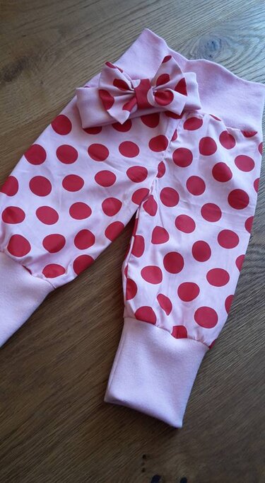 Selbstgenähte rosa Babyhose mit roten Punkten, breiten Bündchen und Schleife auf Holzuntergrund