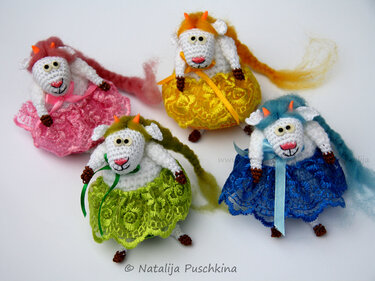 Vier gehäkelte Amigurumi‑Ziegen mit weißen Körpern, bunten Mähnen und Spitzenröcken in Rosa, Gelb, Grün und Blau vor hellem Hintergrund