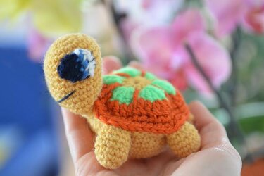 Kleine gehäkelte Amigurumi-Schildkröte mit gelbem Körper und orange-grünem Panzer in einer offenen Hand