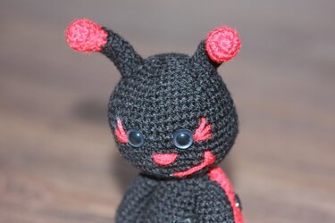 Schwarz-roter Amigurumi-Käfer mit roten Fühlern und freundlichem Gesicht.