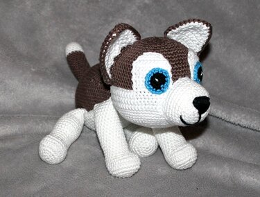 Gehäkeltes Husky-Amigurumi in Braun und Weiß mit blauen Augen auf grauem Hintergrund