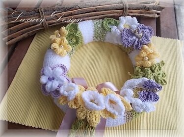 Gehäkelter Türkranz mit Blumen in Weiß, Gelb und Lila sowie grünen Blättern und rosa Band