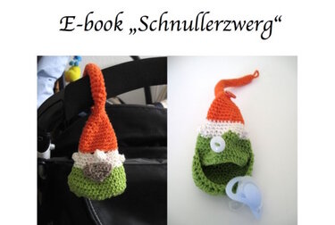 gehäkelter schnullerzwerg mit schlaufe zum befestigen am kinderwagen, schnuller liegt neben dem geöffneten halter