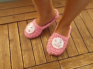 Rosa gehäkelte Ballerina-Pantoffeln mit weißer Tierapplikation auf Holzdielen.
