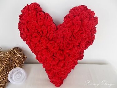 Rotes herzförmiges Kissen aus vielen gehäkelten Rosen auf hellem Untergrund
