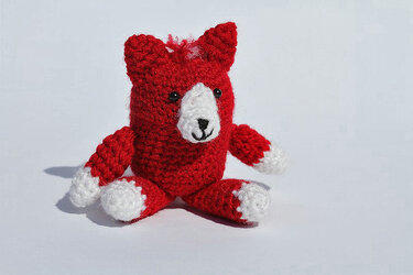 Kleiner roter Amigurumi-Fuchs mit weißen Pfoten und Gesicht, sitzend