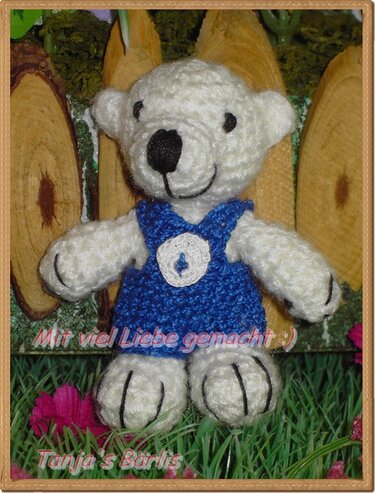 Gehäkelter weißer Teddybär mit blauem Kleid und Knopf vor Holzscheiben
