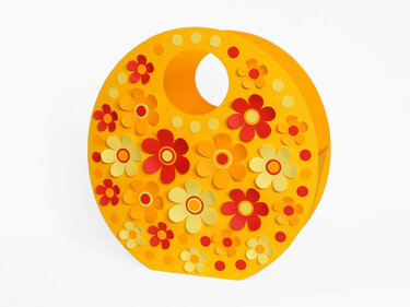 Runde gelbe Papiertüte mit ausgestanztem Henkel und roten, orange und hellgelben Papierblumen