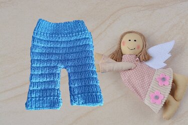 Hellblaue, gestrickte Babyhose mit Rippenmuster neben einer Stoffpuppe mit Fl
Hosen & Strampler