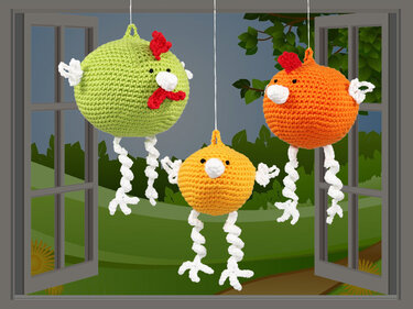 Three colorful crocheted chickens (green, orange, yellow) with white wings and curly legs hanging in a window.
