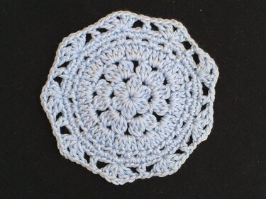 Hellblauer gehäkelter runder Untersetzer mit Blütenmotiv auf dunklem Hintergrund