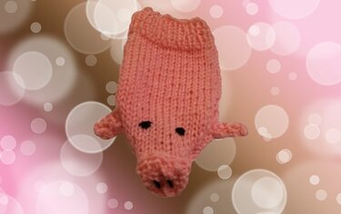 Gestricktes rosa Amigurumi-Schweinchen vor unscharfem, pinken Bokeh-Hintergrund.