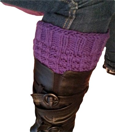 Lila gestrickte Beinstulpen mit Strukturmuster, getragen über schwarzen Stiefeln und blauer Jeans.