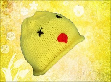 Gelbe gestrickte Babymütze für Babys mit aufgestickten Augen und rotem Munddetail