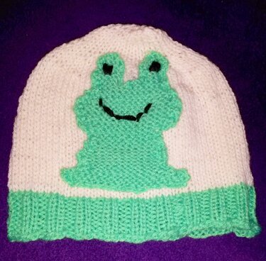 Gestrickte weiße Kindermütze mit hellgrünem Froschaufnäher und grünem Bündchen