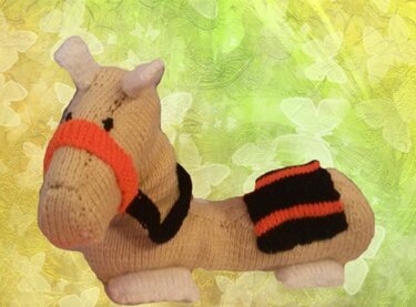 Gestricktes Amigurumi-Pferd beige mit orange-schwarzem Sattel und Zaumzeug