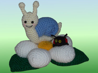 Gehäkelte Amigurumi-Schnecke mit blauem Haus und kleine schwarze Raupe auf weißer gehäkelter Blume