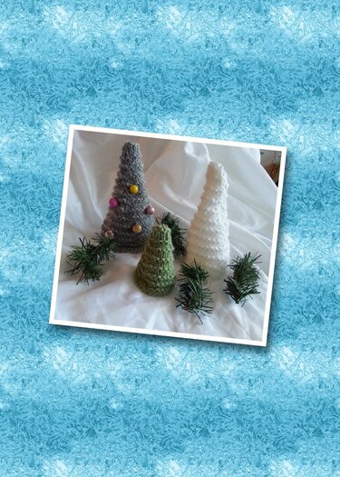 Drei gestrickte Amigurumi-Tannen in Grau, Grün und Weiß; die graue mit bunten Perlen, auf hellem Stoff mit kleinen Tannenzweigen