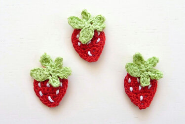 Drei rote gehäkelte Erdbeeren mit grünen Blättern auf weißem Grund.