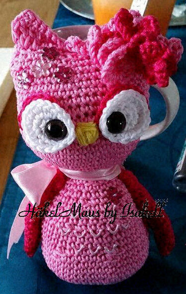 Pink gehäkelte Eulen-Tassenhülle mit weißen Augenringen und rosa Schleife um eine Tasse