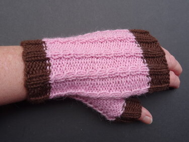 Hand trägt eine gestrickte rosa-braune Armstulpe mit gerippten Bündchen und Strukturmuster.