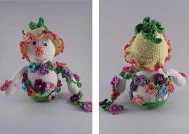 Weißes gehäkeltes Amigurumi mit gelbem Rüschenhut, bunten Häkelblüten und Blumen-Girlande