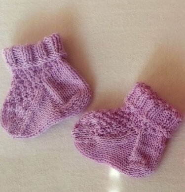 Zwei gestrickte fliederfarbene Babysocken mit Rippenbündchen und Strukturmuster