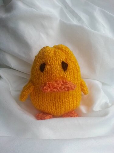 Gestricktes gelbes Küken mit orangefarbenem Schnabel und Füßen auf weißem Stoff