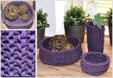 Mehrere violette, gehäkelte Körbe und ein hoher Behälter aus Textilgarn auf einem Holztisch neben Pflanzen.