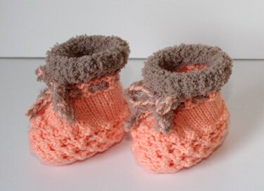 Detailaufnahme von gestrickten Babyschuhen in Pfirsich und Braun mit Zierbändern