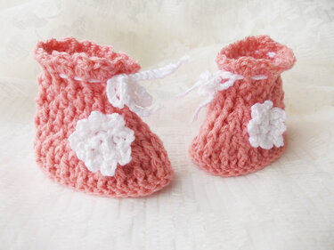 Paar rosa gehäkelte Babyschuhe mit weißen Blumen und weißem Bindeband