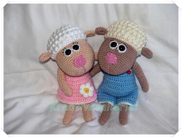 Zwei gehäkelte Amigurumi-Schafe, eins in rosa Kleid mit weißer Blume, eins in blauer Latzhose, beide mit strukturierter Kopfform und großen Augen