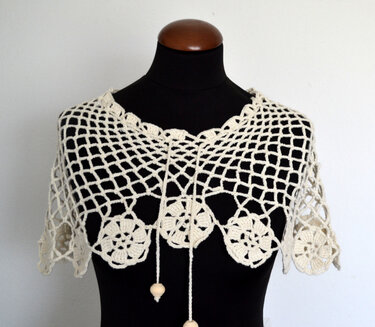 Cremefarbenes Häkelcapelet mit Rautenmuster, Blütenrand und Zugbändern an einer schwarzen Schaufensterpuppe