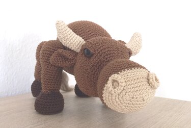 Braunes gehäkeltes Amigurumi-Rind mit hellen Hörnern und heller Schnauze auf hellem Hintergrund
