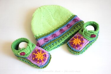 Gestrickte hellgrüne Babymütze mit passenden Babyschuhen, verziert mit lila-gelben Häkelquadraten