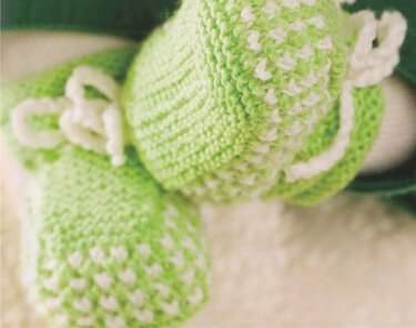 Nahaufnahme zweier gestrickter Babyschuhe in Hellgrün mit weißen Tupfen und Bindebändern