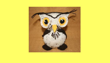 Gestrickte Amigurumi-Eule mit gelben Augen auf braunem Stoff vor gelbem Hintergrund