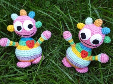 Zwei gehäkelte Amigurumi mit Regenbogenstreifen und Herz im Gras