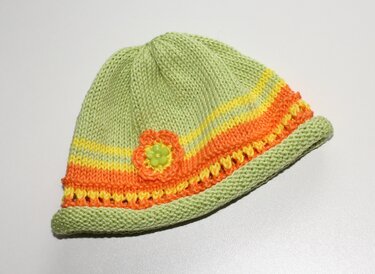 Hellgrüne gestrickte Babymütze mit orange-gelben Streifen und kleiner Blüte