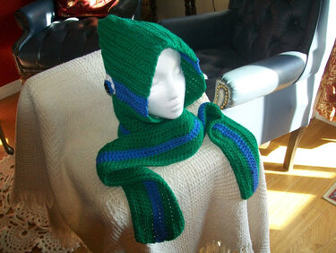 Mannequin wearing a green crocheted hooded scarf with a blue stripe and round button detail