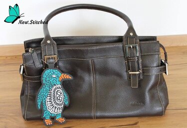 Türkis-oranger Pinguin-Anhänger mit Muster an einer braunen Handtasche