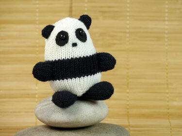 Knitted black and white panda amigurumi sitting on stacked stones