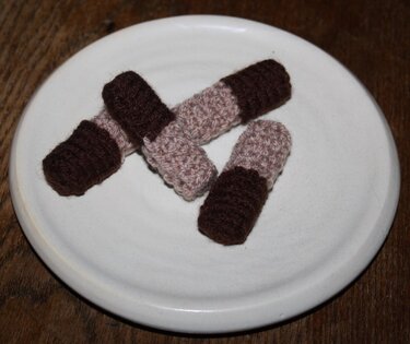 Drei gestrickte kleine Zylinder aus braunem und beigem Garn auf weißem Teller