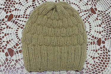 Beige gestrickte Mütze mit Umschlagbündchen auf weißer Häkeldecke